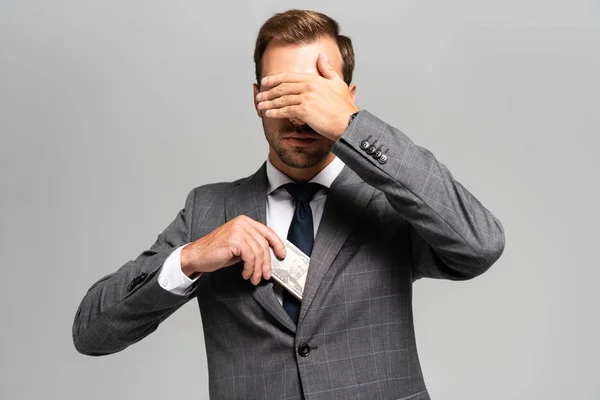 Businessman in suit hiding dollar banknotes and obscuring face isolated on grey — Stock Photo