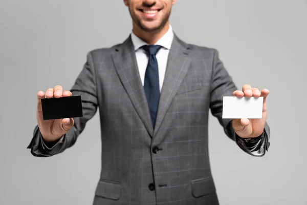 Vista ritagliata di un uomo d'affari sorridente in giacca e cravatta con biglietti da visita isolati su grigio — Foto stock