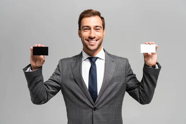 Handsome and smiling businessman in suit holding business cards isolated on grey — Stock Photo