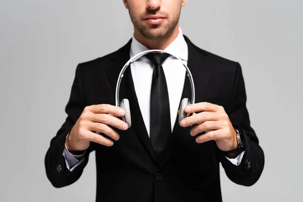 Обрізаний вид бізнесмена в костюмі тримає навушники ізольовані на сірому — стокове фото