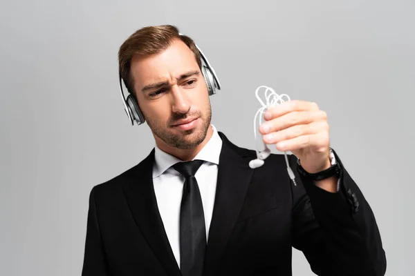 Sad businessman in suit with headphones listening music and looking at earphones isolated on grey — Stock Photo