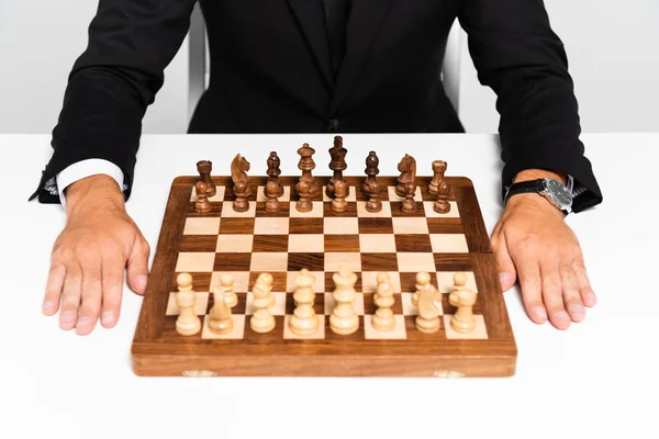 Vista cortada de homem de negócios em terno sentado perto de tabuleiro de xadrez isolado em cinza — Fotografia de Stock