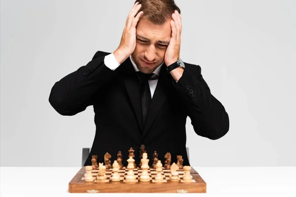 Sad and handsome businessman in suit looking at chessboard isolated on grey — Stock Photo