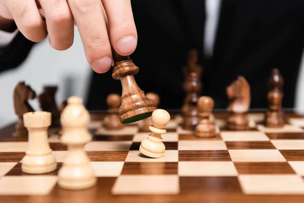 Cropped view of businessman holding chess figure above chessboard — Stock Photo