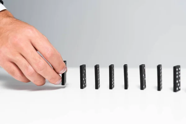 Vista recortada del hombre recogiendo dominó de fila aislado en gris - foto de stock