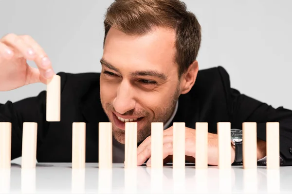 Handsome and smiling businessman in suit picking wooden block from row isolated on grey — Stock Photo