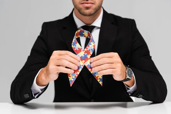 Обрезанный взгляд бизнесмена в костюме, держащего символ аутизма изолированный на сером — стоковое фото