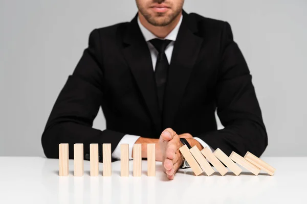 Vista recortada del hombre de negocios en traje evitando que los bloques de madera caigan aislados en gris — Stock Photo