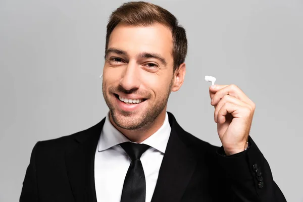 Handsome and smiling businessman in suit holding earphones isolated on grey — Stock Photo