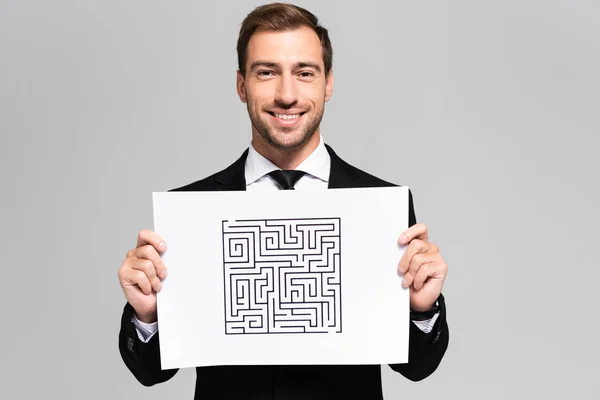 Smiling and handsome businessman holding paper with labyrinth isolated on grey — Stock Photo