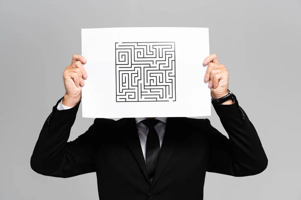 Hombre de negocios oscureciendo la cara con papel con laberinto aislado en gris - foto de stock