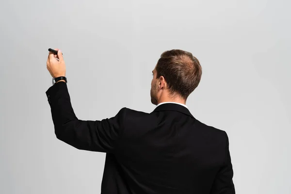 Back view of businessman in suit holding marker isolated on grey — Stock Photo