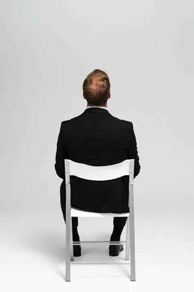 Назад взгляд бизнесмена в костюме, сидящего на стуле на сером фоне — стоковое фото
