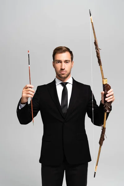 Handsome businessman in suit holding bow and arrow isolated on grey — Stock Photo