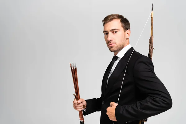 Homem de negócios bonito em terno segurando arco e flechas isoladas em cinza — Fotografia de Stock