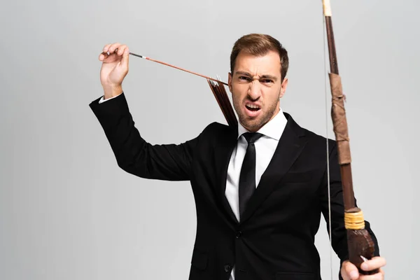 Angry businessman in suit holding bow and arrow isolated on grey — Stock Photo