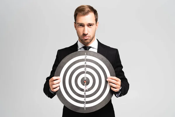 Guapo hombre de negocios en traje sosteniendo dardos tablero aislado en gris - foto de stock