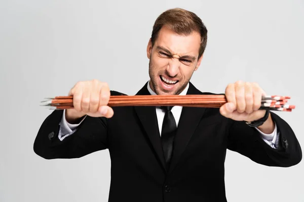 Angry and handsome businessman in suit breaking arrows isolated on grey — Stock Photo