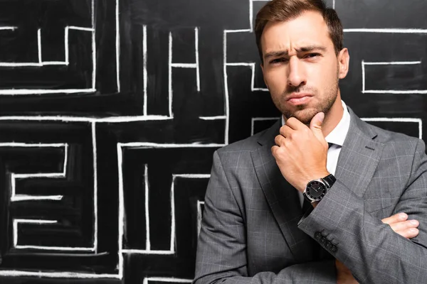 Hombre de negocios guapo y pensativo en traje de pie cerca de laberinto - foto de stock