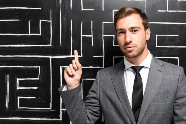 Schöner Geschäftsmann im Anzug steht in der Nähe von Labyrinth und zeigt Idee Zeichen — Stockfoto