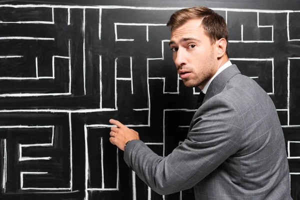 Handsome and shocked businessman in suit pointing with finger at labyrinth — Stock Photo
