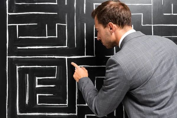 Back view of businessman in suit pointing with finger at labyrinth — Stock Photo