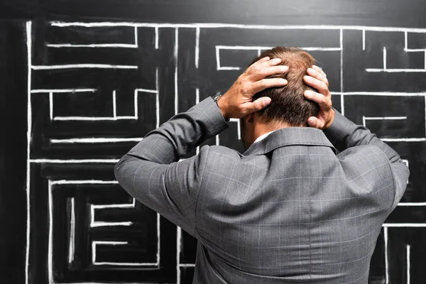 Back view of sad businessman in suit looking at labyrinth and touching head — Stock Photo