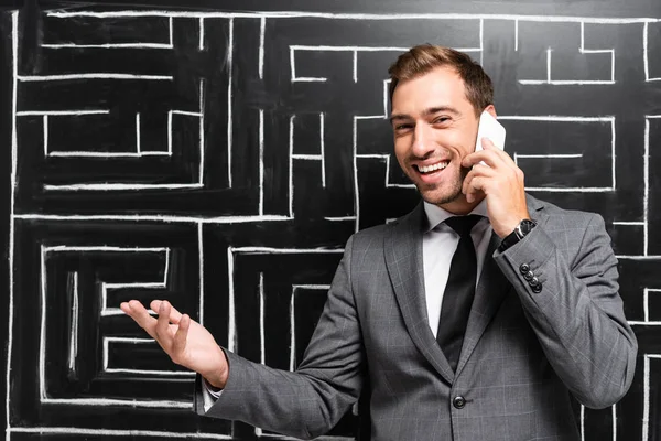 Uomo d'affari bello e sorridente in giacca e cravatta parlare su smartphone e in piedi vicino al labirinto — Foto stock