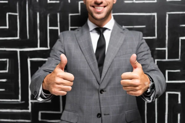 Recortado vista de sonriente hombre de negocios en traje mostrando pulgares hacia arriba cerca de laberinto - foto de stock