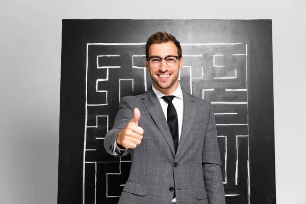 Bonito e sorridente empresário em terno mostrando como e de pé perto do labirinto — Fotografia de Stock
