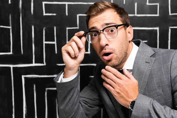 Handsome and shocked businessman in suit looking at camera near labyrinth — Stock Photo