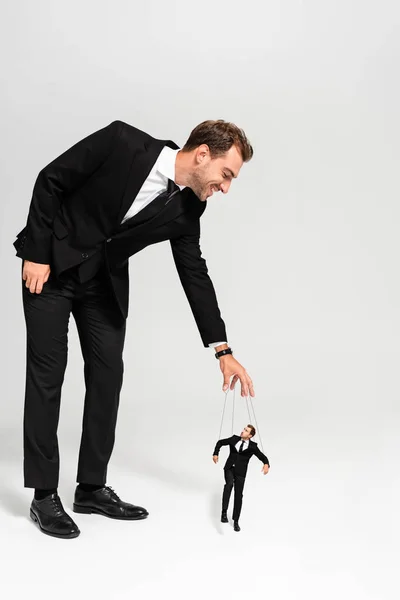 Smiling businessman in suit playing with marionette on grey background — Stock Photo