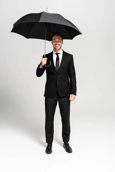Handsome and smiling businessman in suit holding umbrella on grey background — Stock Photo