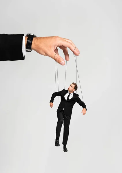 Vista recortada de hombre de negocios jugando con marioneta en traje aislado en gris - foto de stock