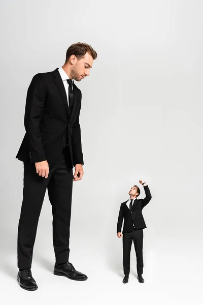 Hombre de negocios en traje mirando marioneta mostrando puño sobre fondo gris - foto de stock