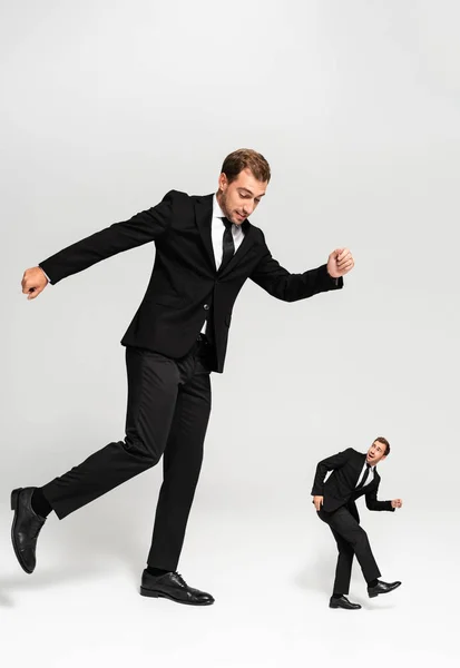 Hombre de negocios enojado en traje golpeando marioneta asustada sobre fondo gris - foto de stock