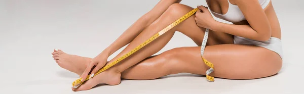 Beautiful slim woman in underwear measuring legs on grey background, panoramic shot — Stock Photo
