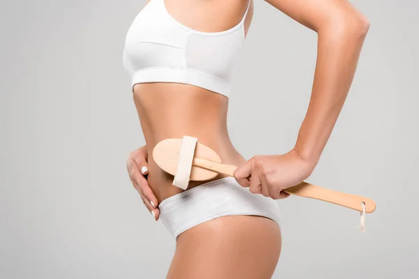 Cropped view of slim woman in underwear massaging body with wooden massage brush isolated on grey — Stock Photo