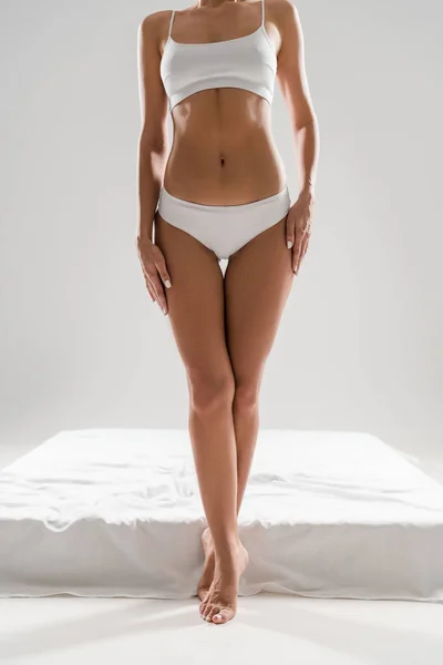 Partial view of beautiful slim woman in underwear standing near bed on tiptoe isolated on grey — Stock Photo