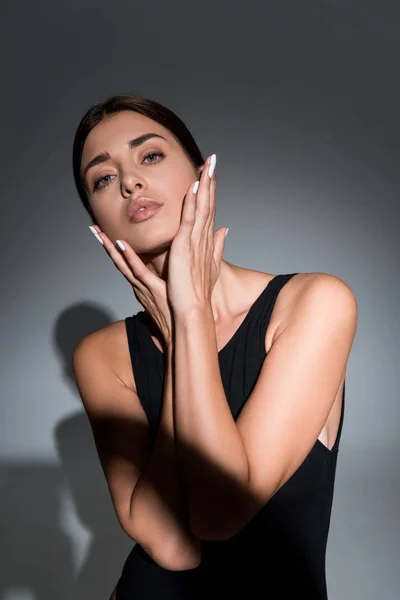 Hermosa joven modelo posando con las manos cerca de la cara sobre fondo negro - foto de stock