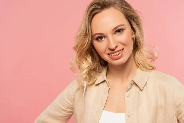 Femme blonde avec des appareils dentaires souriant à la caméra isolée sur rose — Photo de stock