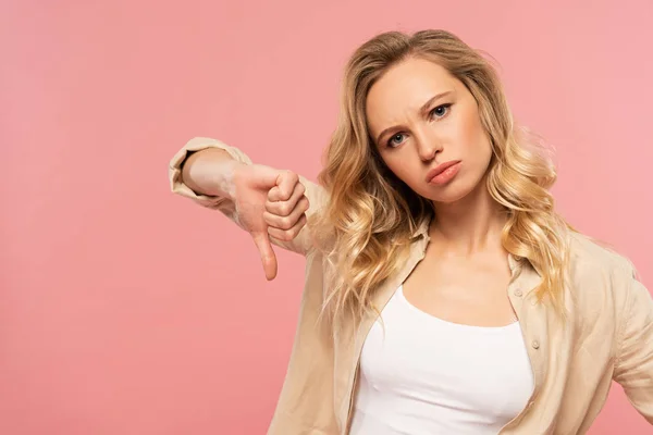 Mujer triste mostrando el pulgar hacia abajo gesto aislado en rosa - foto de stock