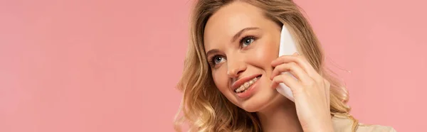 Foto panorámica de una mujer sonriente hablando en un smartphone aislado en rosa - foto de stock