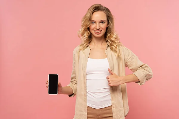 Lächelnde Frau hält Smartphone mit leerem Bildschirm und zeigt Daumen hoch vereinzelt auf rosa — Stockfoto