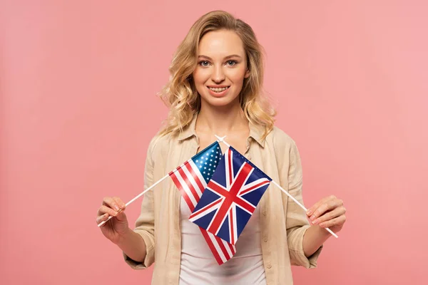 Mujer rubia sonriente sosteniendo banderas americanas y británicas aisladas en rosa - foto de stock