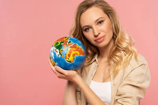 Lächelnde blonde Frau hält Globus isoliert auf rosa — Stockfoto