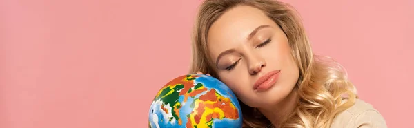 Blonde woman with closed eyes holding globe isolated on pink, panoramic shot — Stock Photo