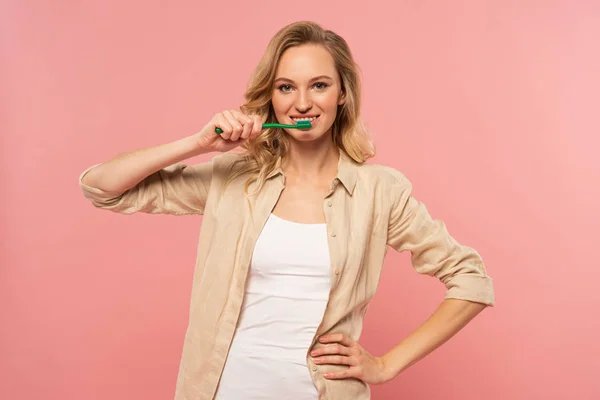 Smiling blonde woman holding toothbrush isolated on pink — Stock Photo