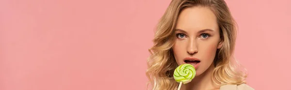 Attractive blonde woman licking lollipop isolated on pink, panoramic shot — Stock Photo