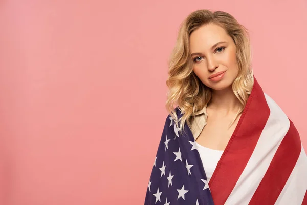 Jeune femme enveloppée dans un drapeau américain isolé sur rose — Photo de stock